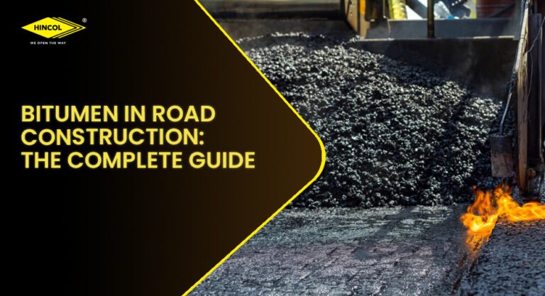 Bitumen road construction in progress with hot asphalt being laid by paving machinery. A black and yellow graphic overlay displays the title “Bitumen in Road Construction: The Complete Guide” alongside the HINCOL logo.
